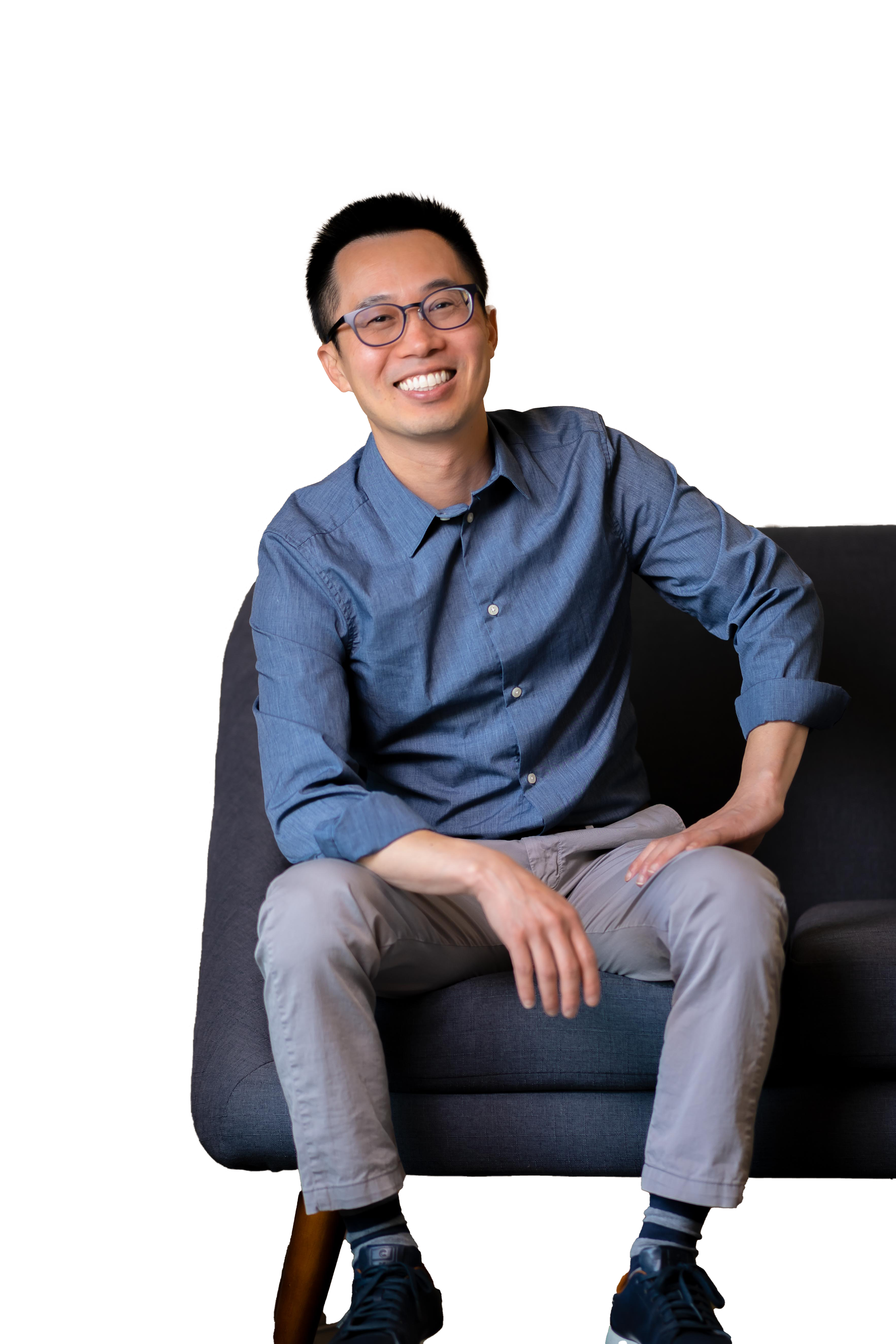 Dr. Chris Pham sitting on the edge of a sofa and smiling.